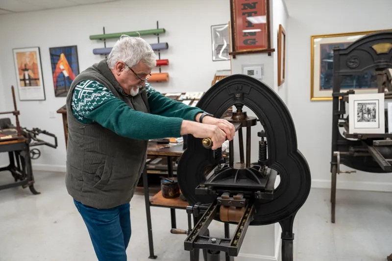 Tata acționând o presă tipografică manuală la Museum of Printing